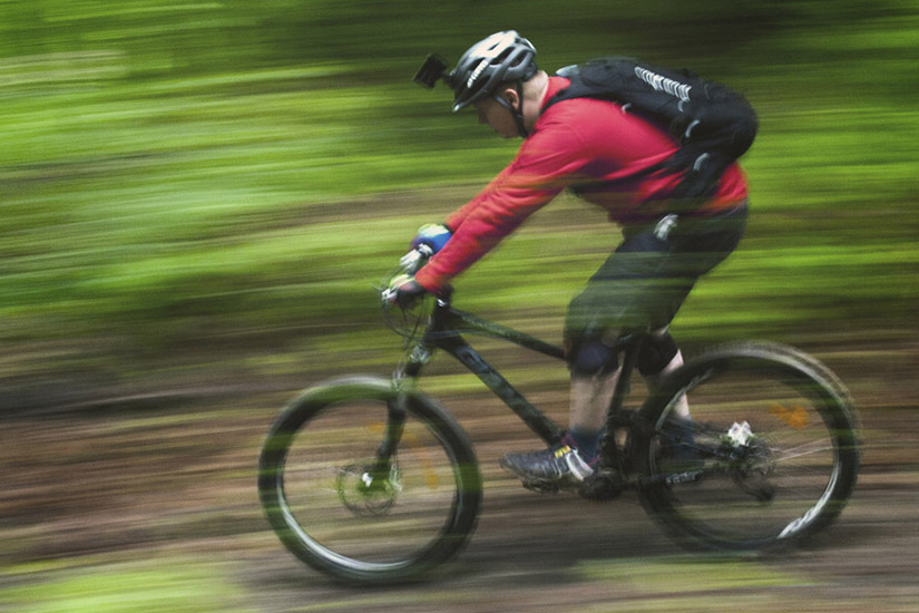 Magyarországi túra: Piros dzsekis, sisakos hozás teker erdei ösvényen, hátizsákkal élvezi a természetjárást és a mozgás örömét. Tekeregj.hu