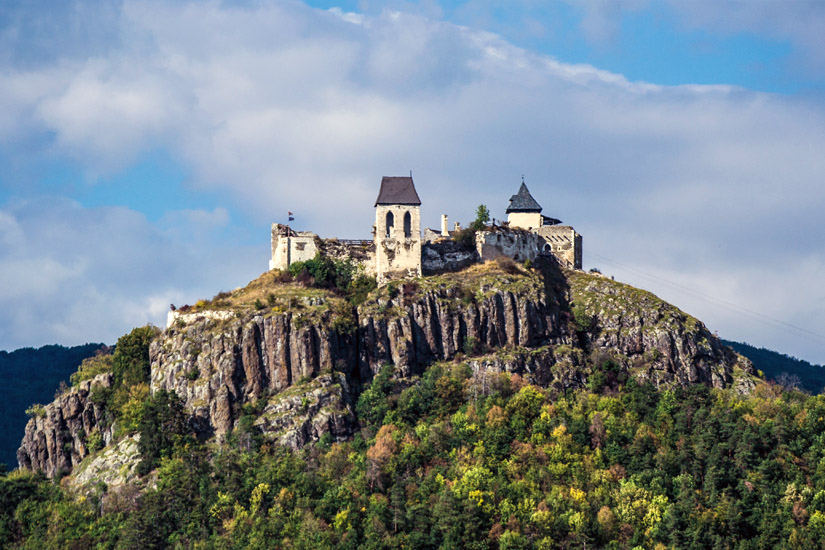 Magyarországi túra: Kővár tornyokkal egy sziklás hegytetőn, zöld erdővel körülvéve, túraútvonal mentén, részben felhős ég alatt. Tekeregj.hu