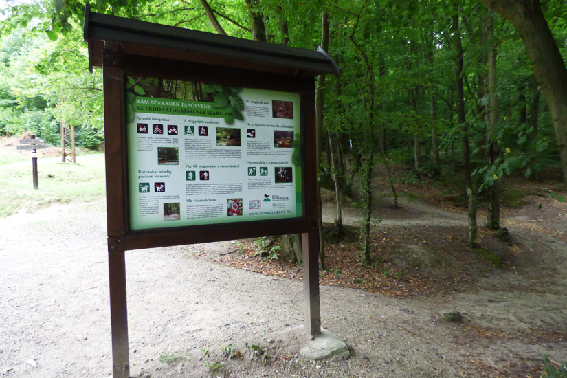 Magyarországi túra: Információs tábla erdei túraösvény bejáratánál, gyalogtúrához és kiránduláshoz, földút vezet a zöld fák közé. Tekeregj.hu