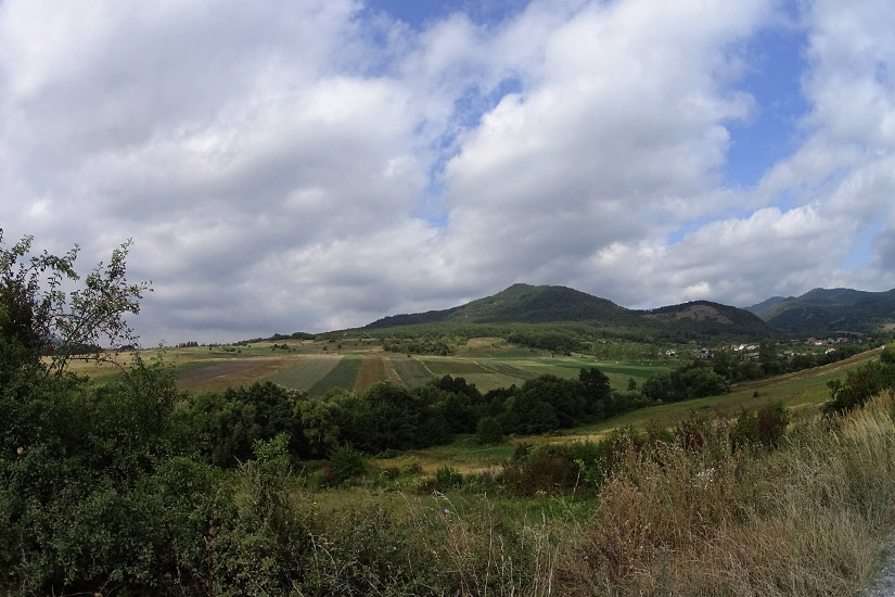 Magyarországi túra: Panoráma vidéki tájra: zöld mezők, fák és dombok, ideális hegyi túrához vagy gyalogtúrához, felhős ég alatt. Tekeregj.hu