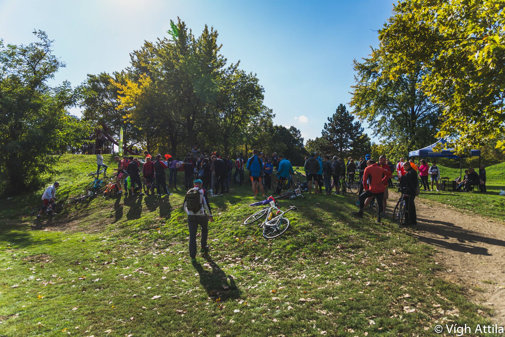 Magyarországi túra: Kerekpáros kirándulók gyűlnek össze egy napos, füves dombon, kerékpárokkal a zöld fák között. Tekeregj.hu