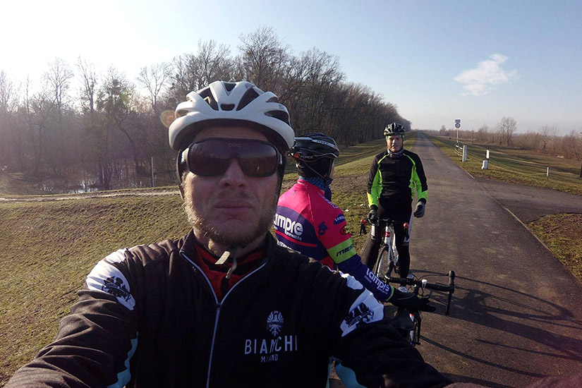 Magyarországi túra: Három kerékpáros sisakban és sportruhában szelfit készít túra közben, fák és mező között, aszfaltos úton. Tekeregj.hu