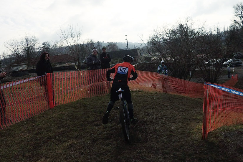 Magyarországi túra: Kerékpáros 127-es mezben, bukósisakban teker fel egy füves ösvényen panorámás kilátással, nézők a háló mögött. Tekeregj.hu