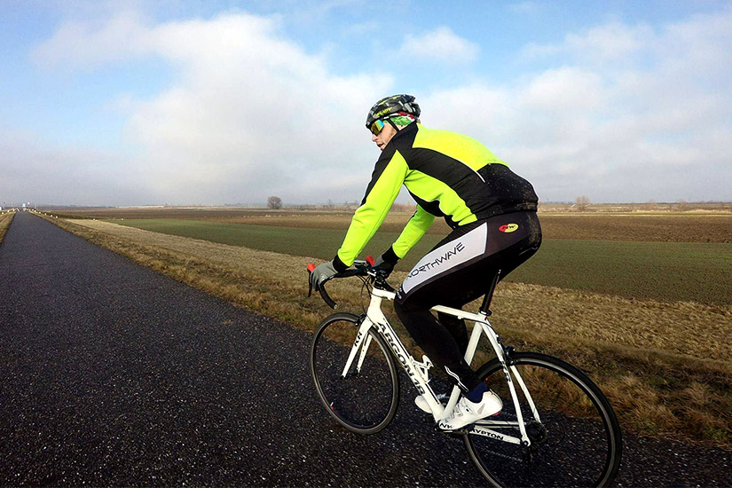 Magyarországi túra: Kerékpáros neon sárga-fekete dzsekiben teker sík tájon, felhős ég alatt; ideális hozásra vagy természetjárásra. Tekeregj.hu