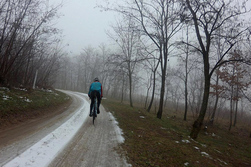 Magyarországi túra: Kerékpáros teker egy kanyargós, sáros úton, kopár, ködös erdőben; havases jeges foltok természetjáráson. Tekeregj.hu