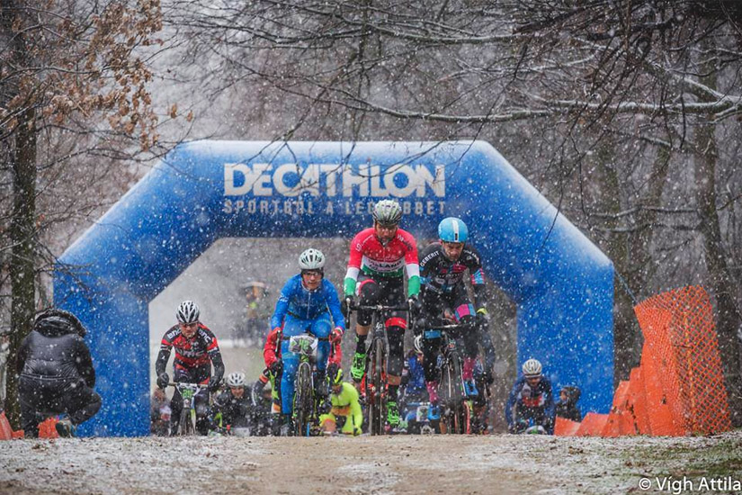 Magyarországi túra: Kerékpárosok tekernek havas időben a Decathlon kapu alatt, természetjárás hangulatban, nézőkkel és fák között. Tekeregj.hu