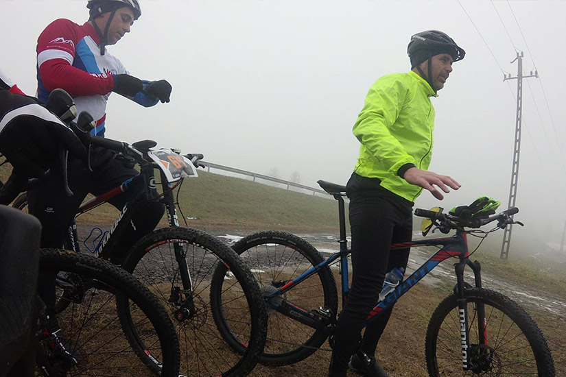 Magyarországi túra: Két kerékpáros sisakban, sportöltözetben, ködös napon hegyi túrára készül; egyikük sárga dzsekit visel. Tekeregj.hu