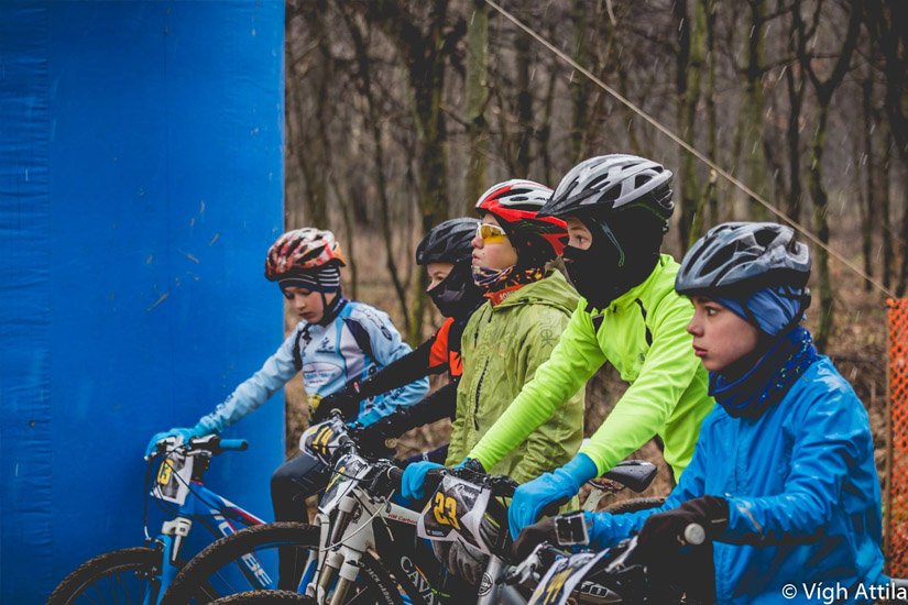 Magyarországi túra: Téli bringás gyerekek sorakoznak a rajtvonalnál, nagy kék kapunál, tekeregj kaland indul az erdőben. Tekeregj.hu