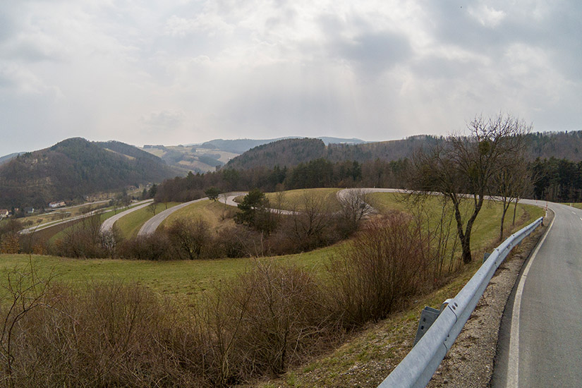 Magyarországi túra: Kanyargó út dombos tájon, fűvel, fákkal, bokrokkal; ideális természetjárásra vagy kerékpártúrára a vidéken. Tekeregj.hu