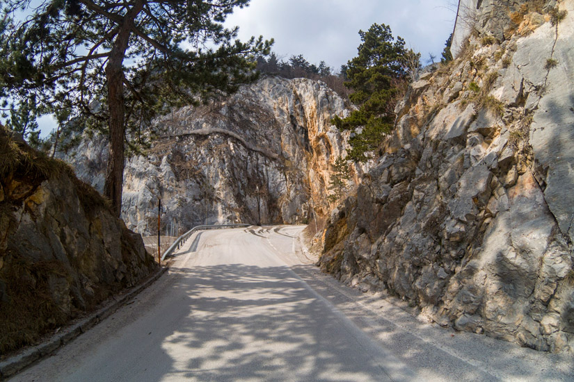 Magyarországi túra: Kanyargó út sziklák és fenyők között, részben felhős ég alatt - ideális természetjáráshoz vagy hegyi túrához. Tekeregj.hu