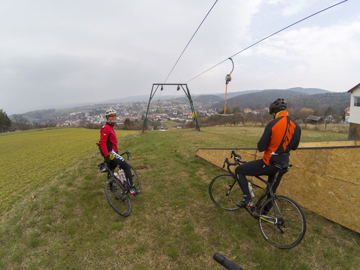 Magyarországi túra: Kerékpárosok sisakban, pihenő a dombon, kilátással városra és hegyekre, sífelvonóval a háttérben, természetjárás. Tekeregj.hu