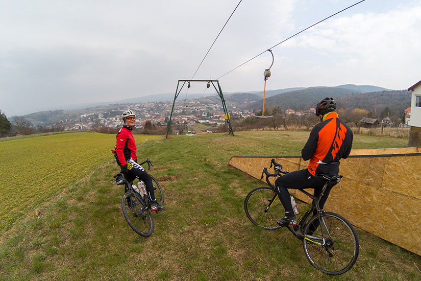 Magyarországi túra: Két biciklis sisakban és felszerelésben pihen egy füves hegyoldalon, háttérben kisváros és sífelvonó Miskolc környékén. Tekeregj.hu