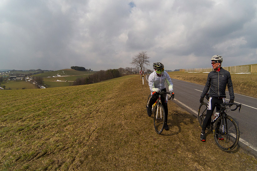 Magyarországi túra: Két biciklis sisakban vidéki úton pihen, háttérben dombok, kopár fák és felhős ég. Ideális hegyi kerékpártúrához. Tekeregj.hu