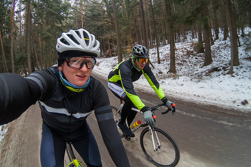 Magyarországi túra: Két kerékpáros bukósisakban és napszemüvegben teker havas erdei úton, téli tájban, kellemes kirándulás közben. Tekeregj.hu