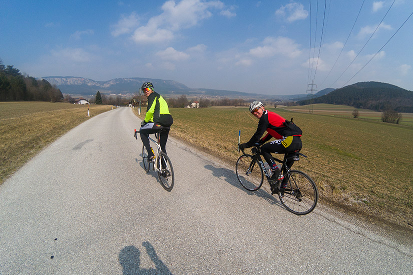 Magyarországi túra: Két kerékpáros tekercs vidéki úton dombok közt, bukósisakban, sportfelszerelésben, természetjárás közben. Tekeregj.hu