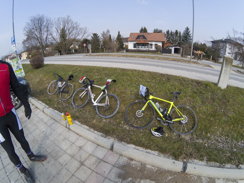 Magyarországi túra: Négy országúti kerékpár parkol füves út szélén járda mellett, tekeregjhez vagy természetjáráshoz. Háttérben házak, fák. Tekeregj.hu