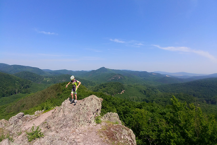 Magyarországi túra: Bukósisakos túrázó sziklás kilátón, panoráma erdőkre és dombokra, tiszta ég alatt - emlékezetes hegyi túra. Tekeregj.hu