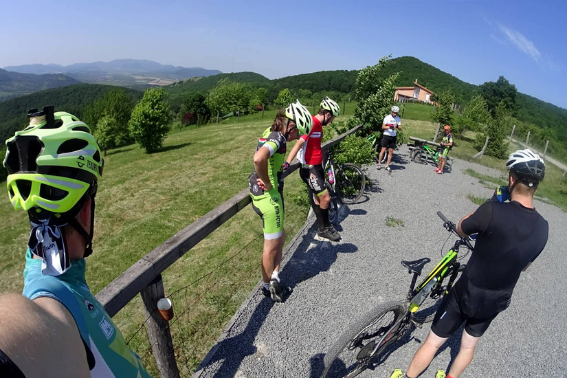 Magyarországi túra: Kerékpárosok pihennek egy hegyi túrán, zöld dombok között, kavicsos úton, tiszta kék ég alatt. Tekeregj.hu