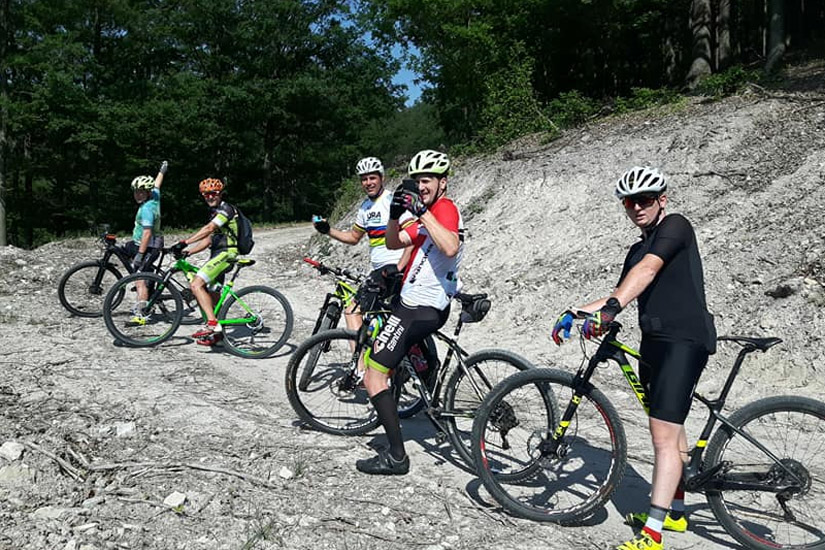 Magyarországi túra: Négy kerékpáros sisakban megpihen egy erdei, köves ösvényen kirándulás közben, napsütéses időben. Tekeregj.hu