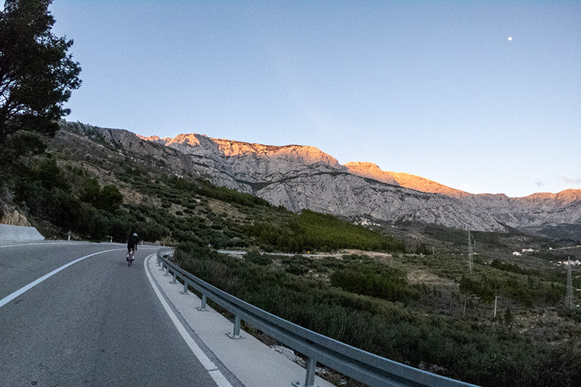 Magyarországi túra: Kerékpáros teker hegyi szerpentinen naplementében, arany fényben fürdő csúcsok és lenyűgöző panoráma tiszta ég alatt. Tekeregj.hu