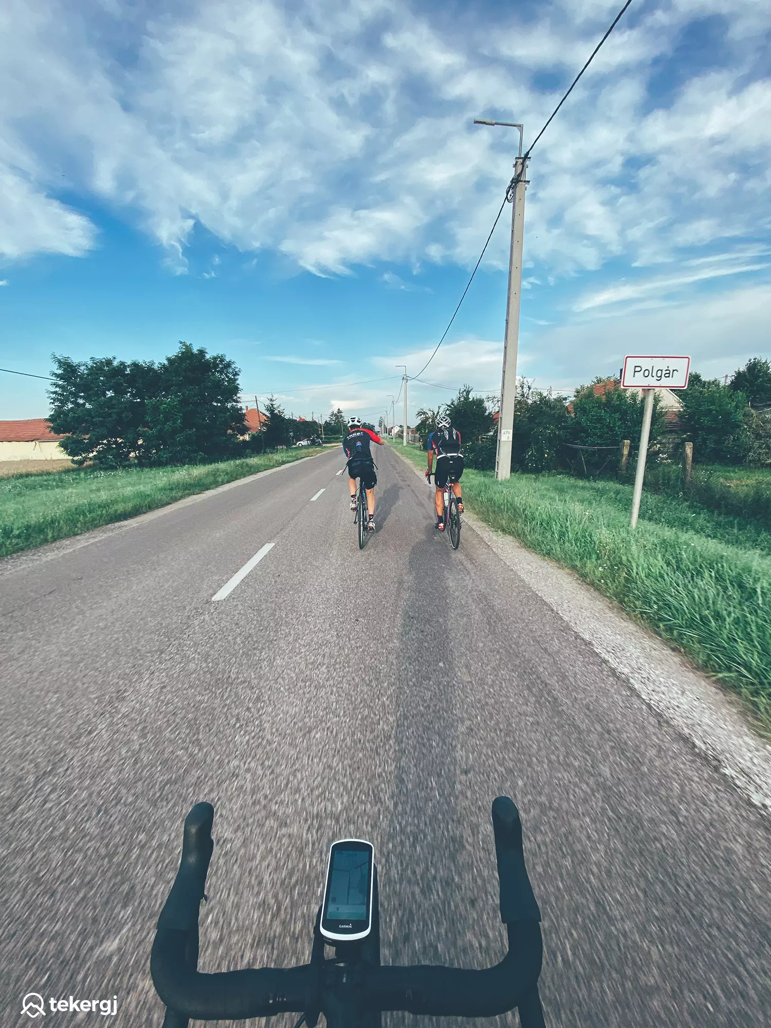 Magyarországi túra: Három kerékpáros teker Polgár felé vidéki úton, természetjárás alatt, napos-felhős időben, zöld növényzet mellett. Tekeregj.hu