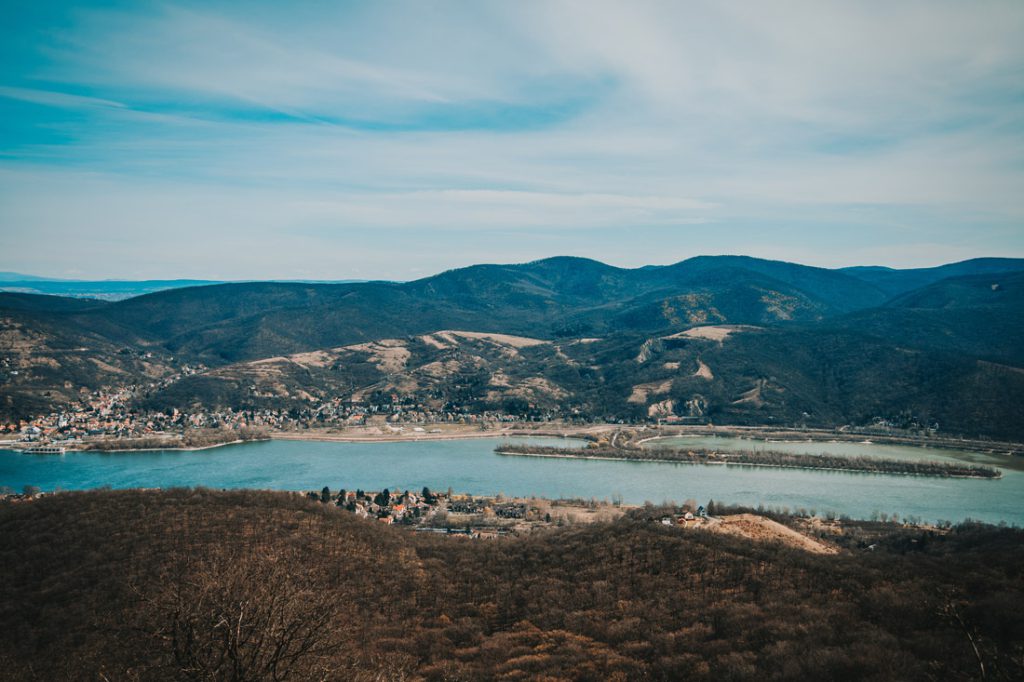 Magyarországi túra: Széles folyó kanyarog az erdős hegyek között, panorámás kilátás gyalogtúrán, kisvárosok a víz mentén, felhős ég alatt. Tekeregj.hu