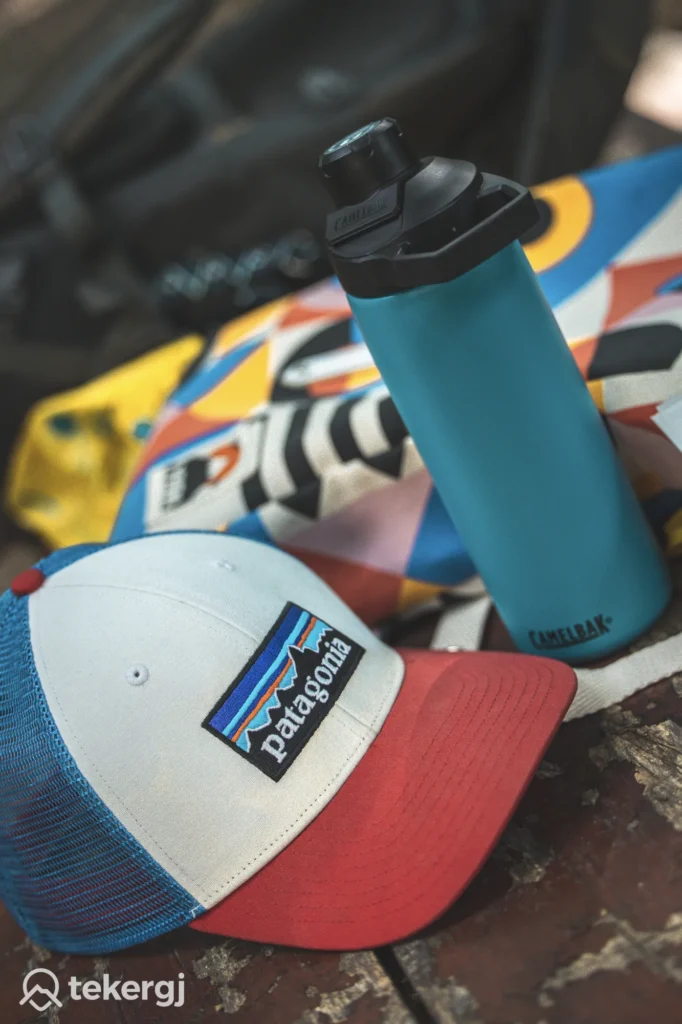Magyarországi túra: Patagonia sapka és kék CamelBak kulacs színes táskán hegyi túrához, fapadon elhelyezve. Tekeregj.hu