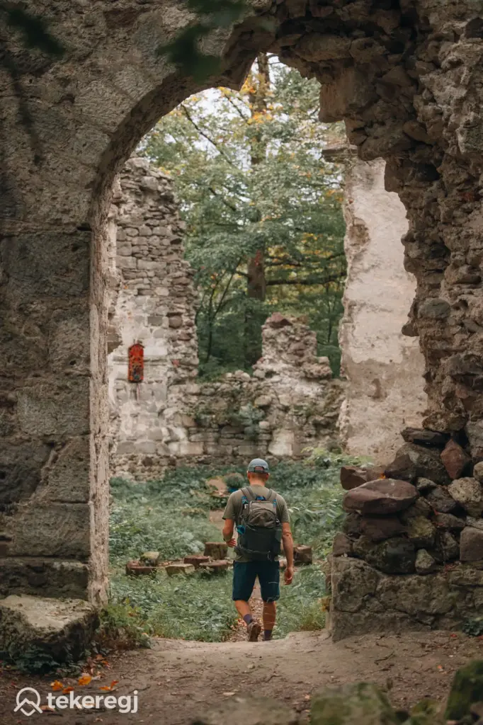 Magyarországi túra: Hátizsákos túrázó áll egy romos kőépületben, körülötte zöld növényzet és fák, gyalogtúra panorámás helyszínen. Tekeregj.hu