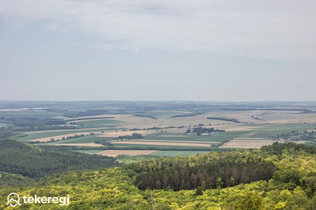 Magyarországi túra: Panoráma vidéki tájról, zöld erdők és mezők alatt felhős ég. Ideális hegyi túrázáshoz, bal alsó sarokban Tekeregj logó. Tekeregj.hu