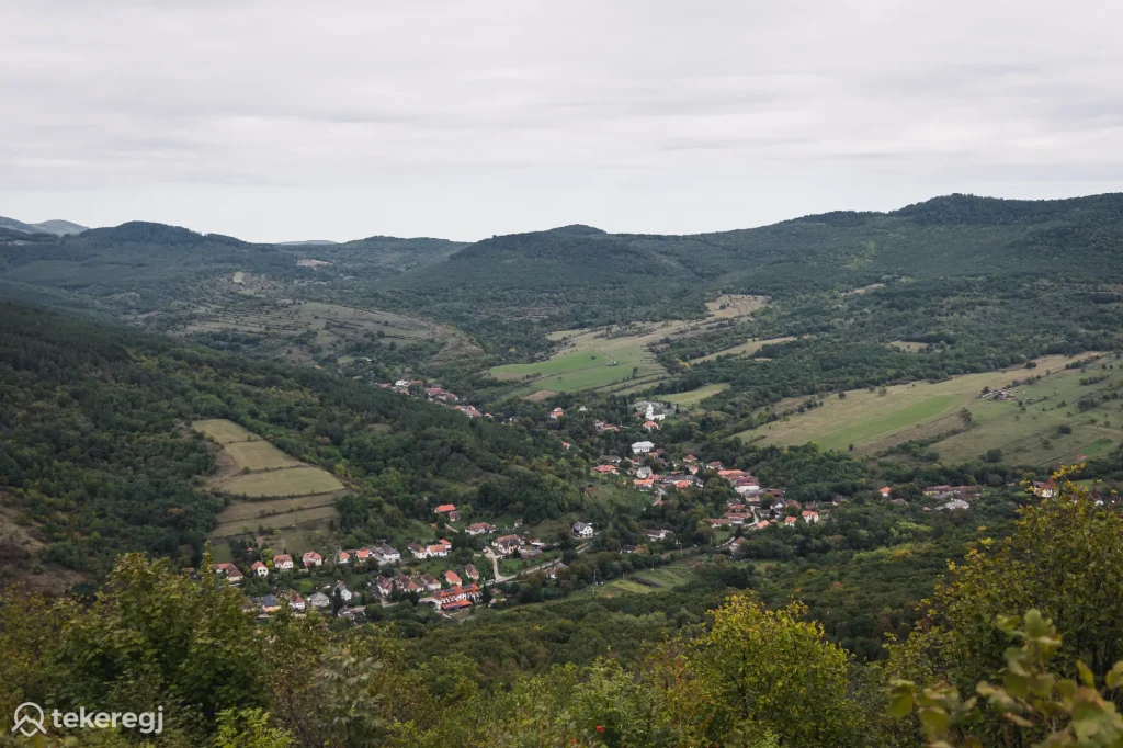 Magyarországi túra: Vörös tetős falucska zöld völgyben, erdőkkel és mezőkkel, felhős ég alatt; "tekeregj" túra logó a sarokban. Tekeregj.hu