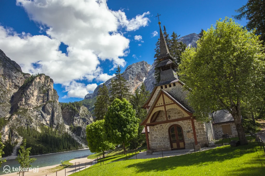 Magyarországi túra: Egy kis kőkápolna a Lago di Braies mellett, a Dolomitokban; zöld fák, hegyek és kék ég – ideális hely túrázásra. Tekeregj.hu