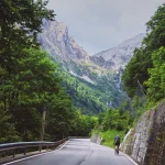 Magyarországi túra: Egy kerékpáros halad a kanyargós Plöckenpass úton az Alpokban, zöld erdők és sziklás hegycsúcsok között. Tekeregj.hu
