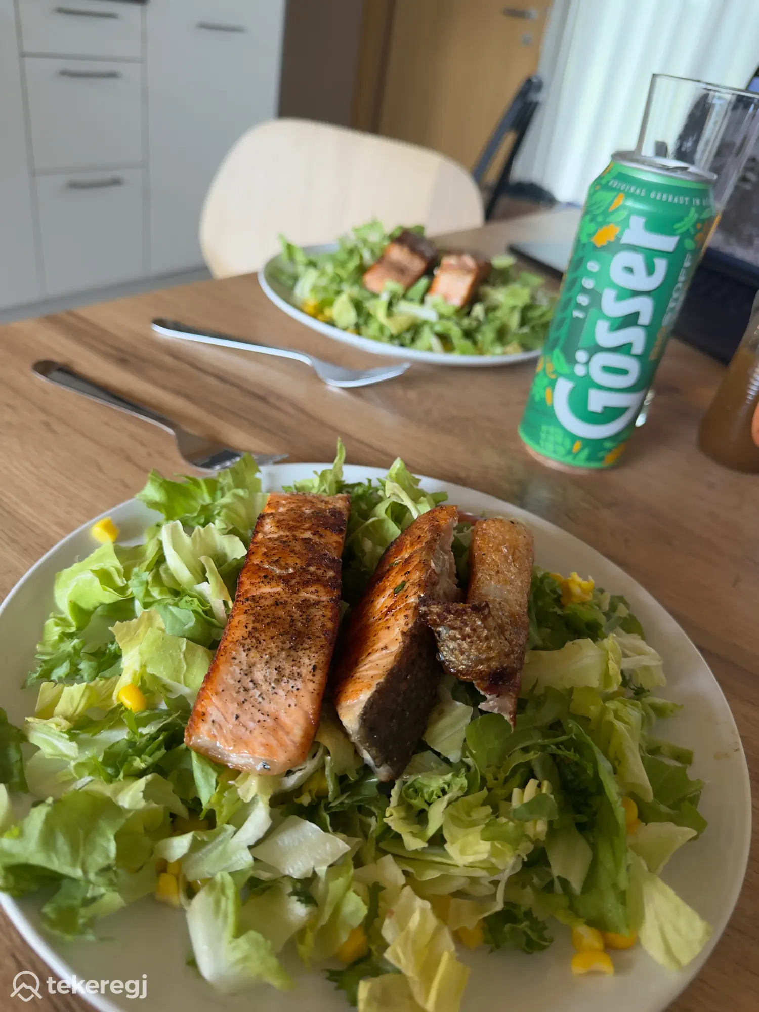 Tekeregj túra: Grillezett lazacos saláta sárga paprikával, mellette egy Gösser sör egy fapadon, a háttérben egy második tányér és ital – ideális frissítő ebéd túra vagy kerékpározás közben alpesi környezetben. Tekeregj.hu